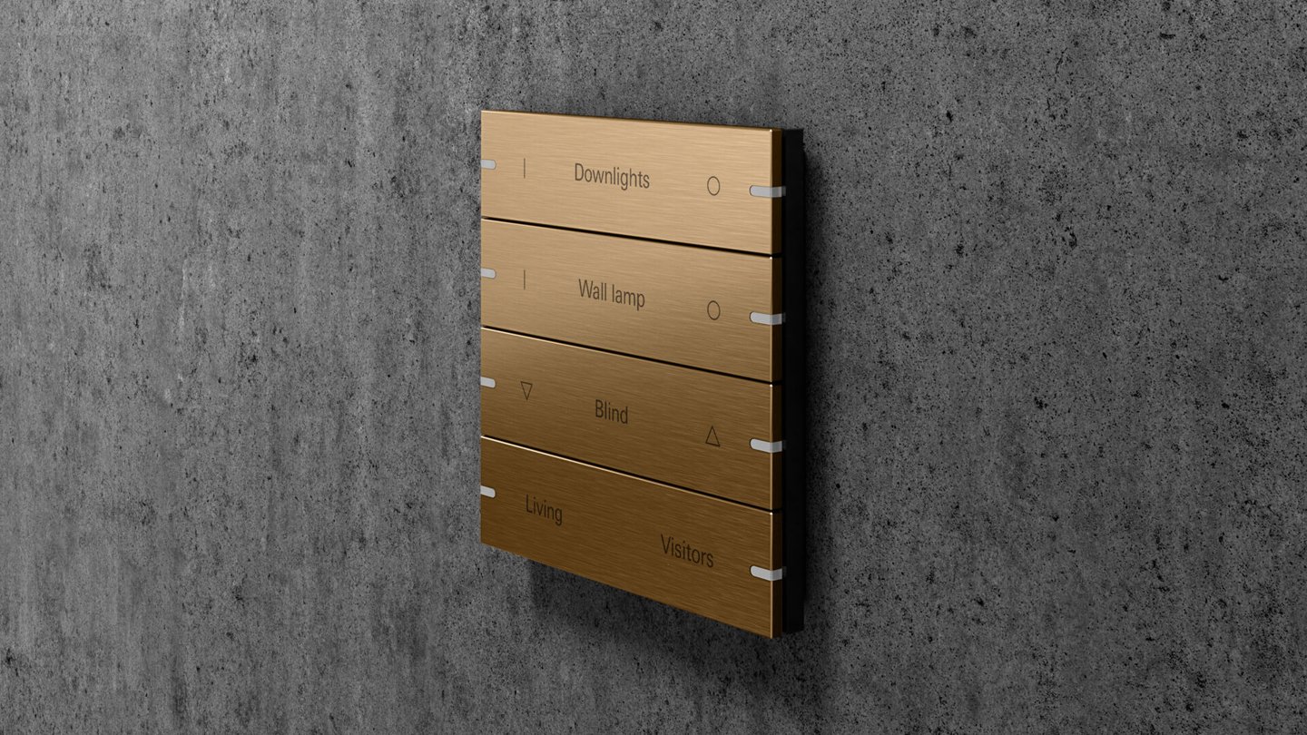 Botoneira de domótica em bronze numa parede de betão, com comandos para luzes, estores e cenários
